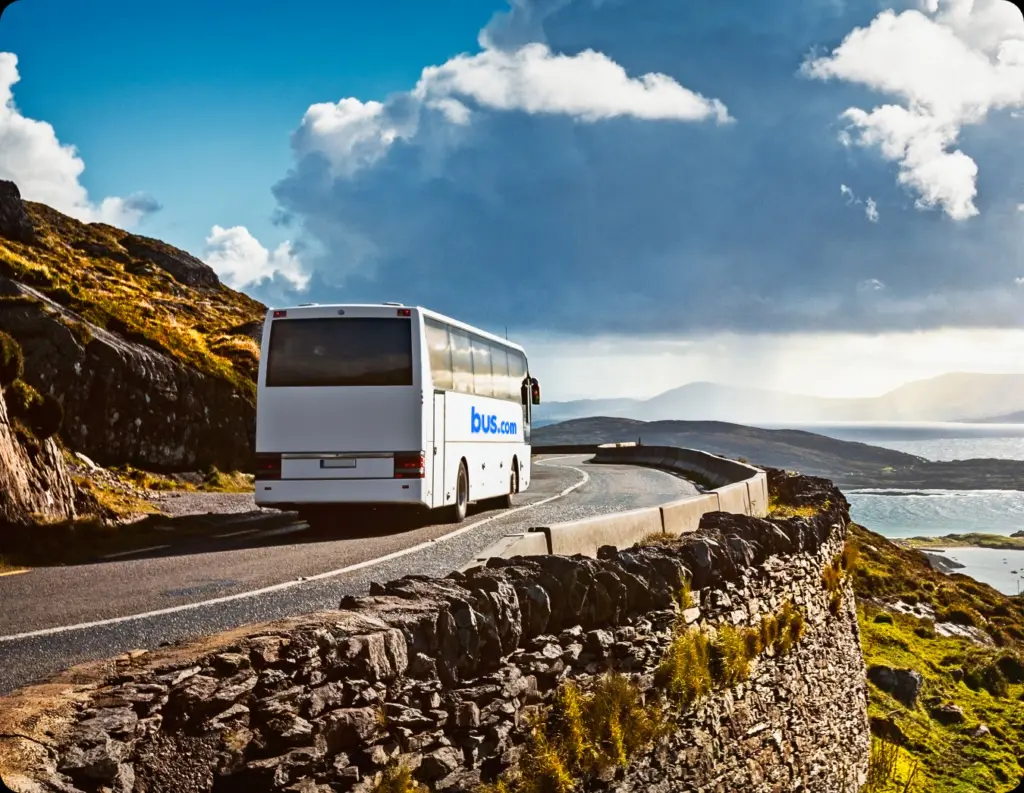 A sustainable Bus.com charter bus drives down a coastal highway